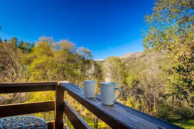 two coffee mugs sitting on a wooden rail on a balcony at Sierra Vista Lookout Lodge with Creek, Waterfall and Waterholes, minutes from Bass Lake and Yosemite South Gate in North Fork